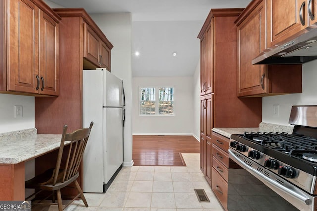 kitchen with light tile patterned floors, built in desk, light stone countertops, gas stove, and white fridge