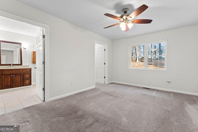 unfurnished bedroom featuring ceiling fan, light colored carpet, sink, and ensuite bath