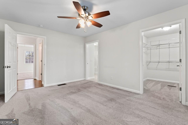 unfurnished bedroom featuring ensuite bathroom, a spacious closet, light colored carpet, ceiling fan, and a closet