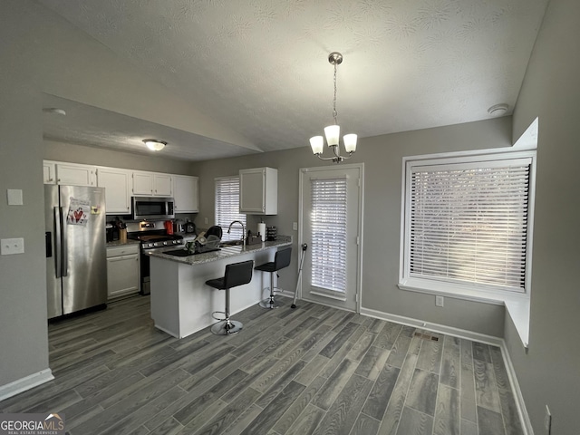 kitchen with appliances with stainless steel finishes, decorative light fixtures, a breakfast bar area, white cabinets, and kitchen peninsula