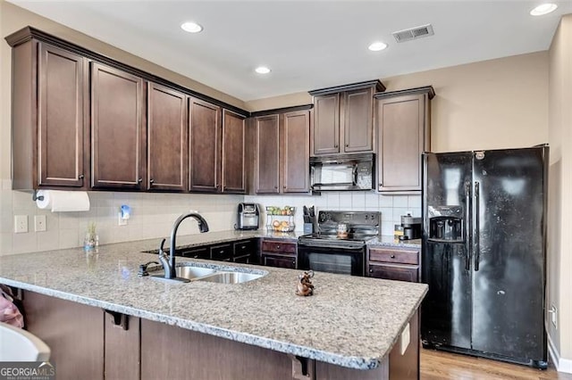 kitchen with light stone counters, kitchen peninsula, sink, and black appliances