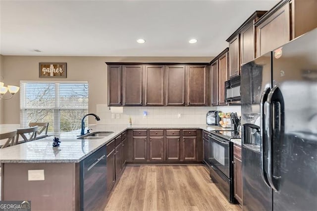 kitchen with light stone counters, kitchen peninsula, sink, and black appliances