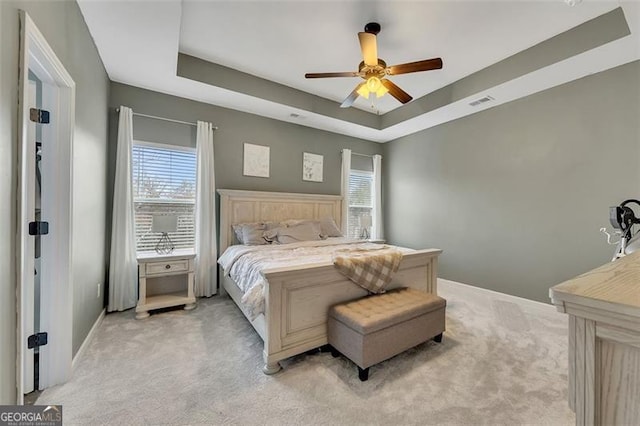 carpeted bedroom with ceiling fan and a raised ceiling