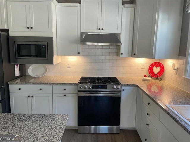 kitchen with white cabinetry, appliances with stainless steel finishes, dark hardwood / wood-style flooring, light stone countertops, and decorative backsplash