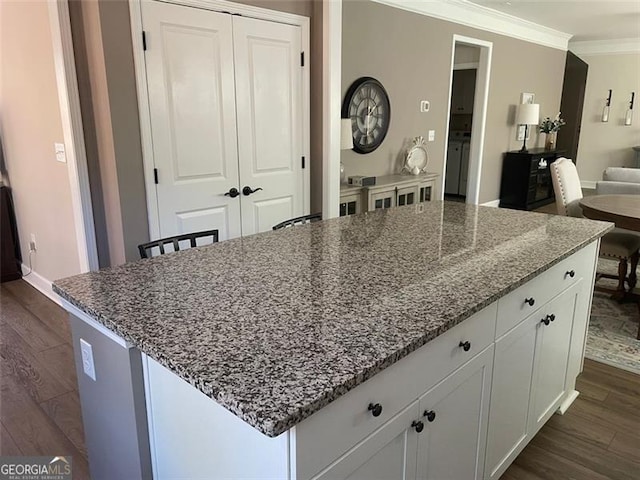 kitchen featuring white cabinetry, ornamental molding, dark hardwood / wood-style floors, a kitchen island, and light stone countertops