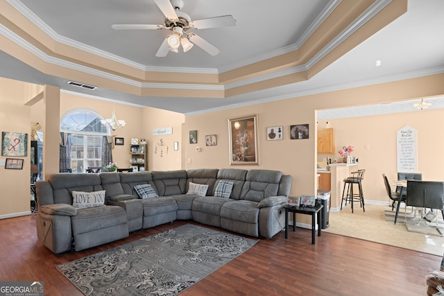 living room with a tray ceiling, dark wood-type flooring, and ceiling fan with notable chandelier