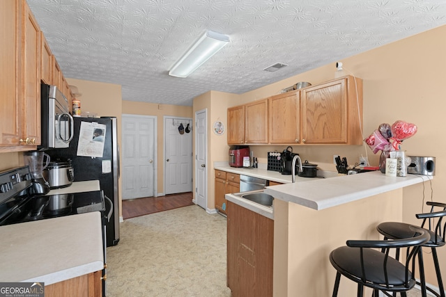 kitchen with light brown cabinetry, sink, a kitchen breakfast bar, kitchen peninsula, and stainless steel appliances