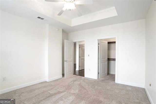 unfurnished bedroom featuring ceiling fan, a raised ceiling, carpet, and a walk in closet