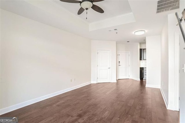 unfurnished room with ceiling fan, a tray ceiling, and dark hardwood / wood-style flooring