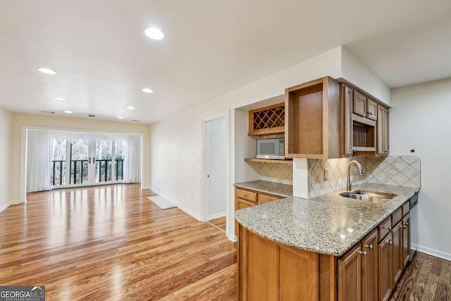 kitchen with tasteful backsplash, sink, light stone counters, and light hardwood / wood-style floors