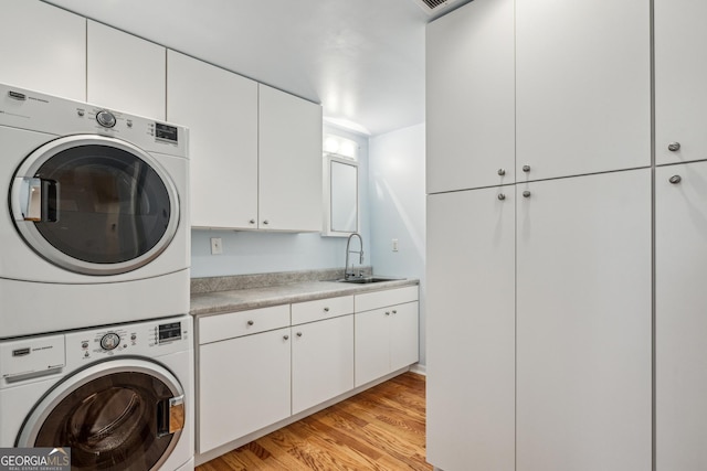 laundry room with stacked washer and dryer, sink, cabinets, and light hardwood / wood-style flooring