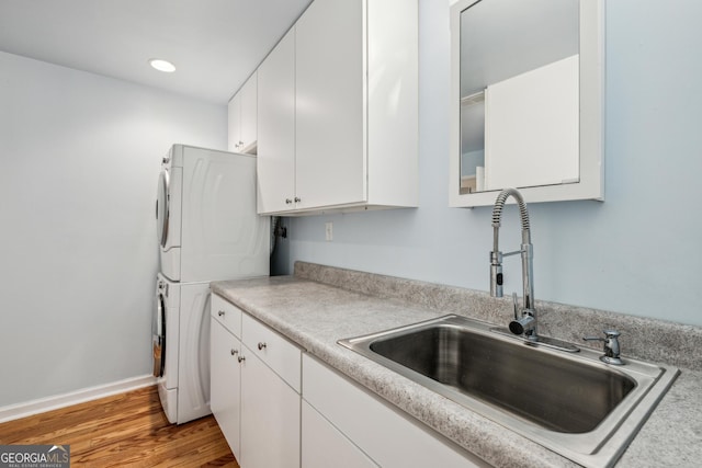 kitchen with light wood-type flooring, stacked washer / drying machine, sink, and white cabinets