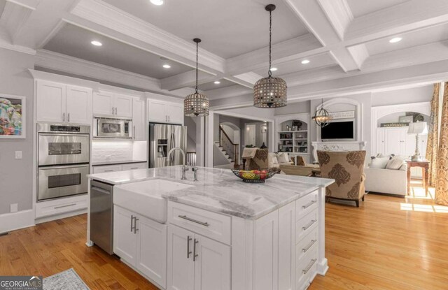 kitchen with decorative light fixtures, an island with sink, sink, white cabinets, and stainless steel appliances