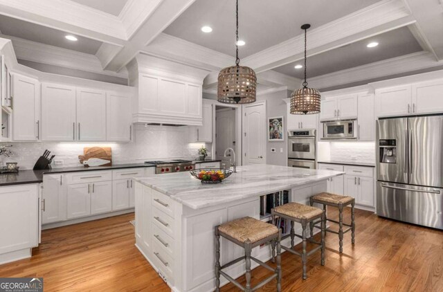 kitchen with appliances with stainless steel finishes, pendant lighting, an island with sink, dark stone countertops, and a kitchen breakfast bar