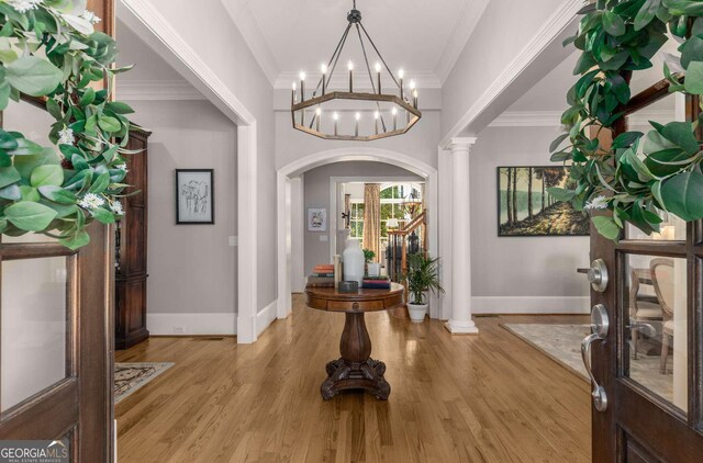 entrance foyer featuring ornate columns, ornamental molding, an inviting chandelier, and light hardwood / wood-style flooring