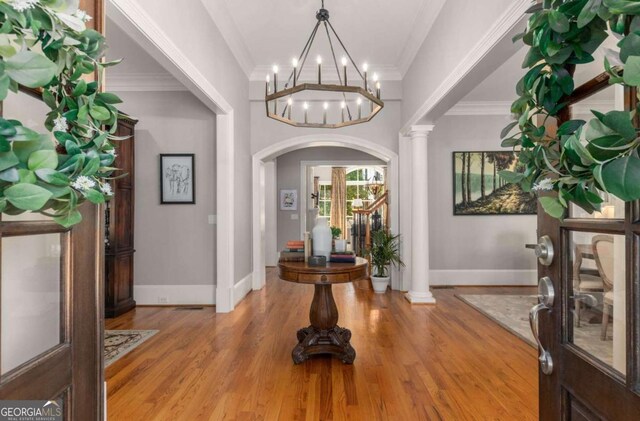 foyer entrance featuring decorative columns, crown molding, a chandelier, and light wood-type flooring