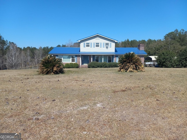 traditional-style house with a chimney, metal roof, and a front yard