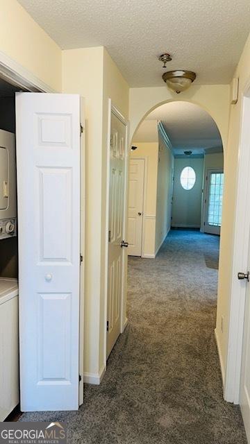 hallway featuring stacked washer / dryer, dark carpet, and a textured ceiling