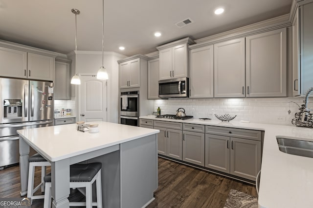 kitchen featuring a breakfast bar area, appliances with stainless steel finishes, gray cabinetry, dark hardwood / wood-style floors, and decorative light fixtures