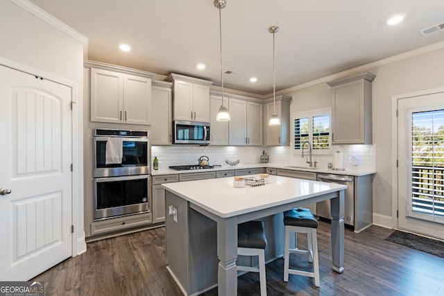 kitchen featuring pendant lighting, appliances with stainless steel finishes, gray cabinetry, a kitchen breakfast bar, and a kitchen island