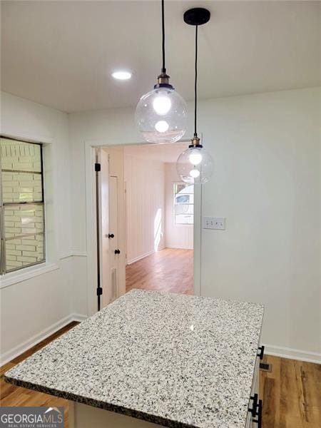 kitchen with wood-type flooring, a center island, pendant lighting, and light stone counters