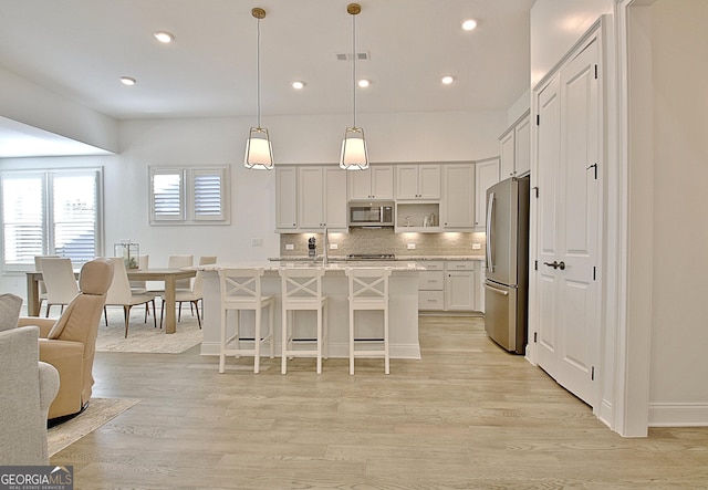 kitchen featuring a breakfast bar, appliances with stainless steel finishes, a kitchen island with sink, tasteful backsplash, and decorative light fixtures