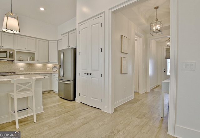 kitchen with appliances with stainless steel finishes, decorative light fixtures, white cabinets, a kitchen breakfast bar, and light hardwood / wood-style flooring