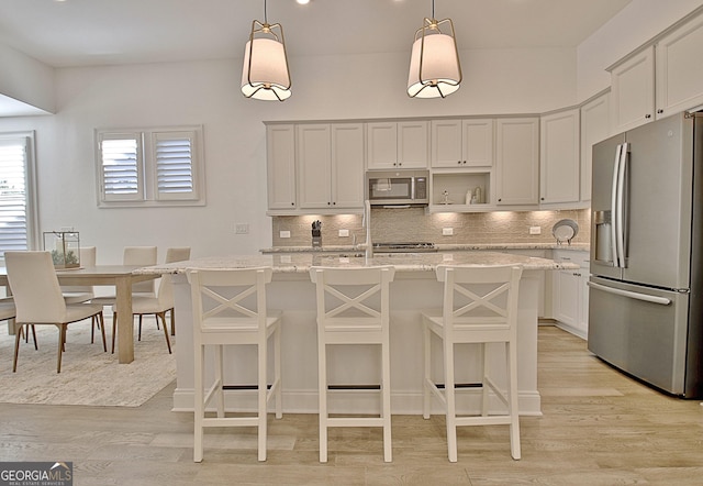 kitchen featuring light stone counters, hanging light fixtures, stainless steel appliances, and an island with sink