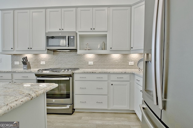 kitchen with appliances with stainless steel finishes, white cabinetry, backsplash, light stone counters, and light hardwood / wood-style flooring