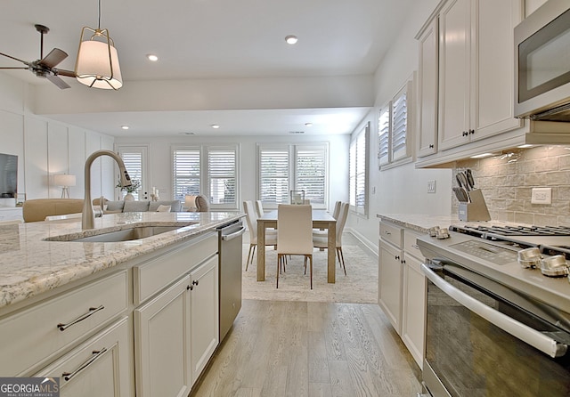 kitchen with decorative light fixtures, sink, light stone counters, stainless steel appliances, and a healthy amount of sunlight