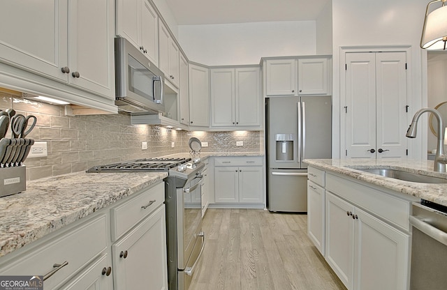 kitchen featuring sink, light hardwood / wood-style flooring, appliances with stainless steel finishes, white cabinets, and decorative backsplash