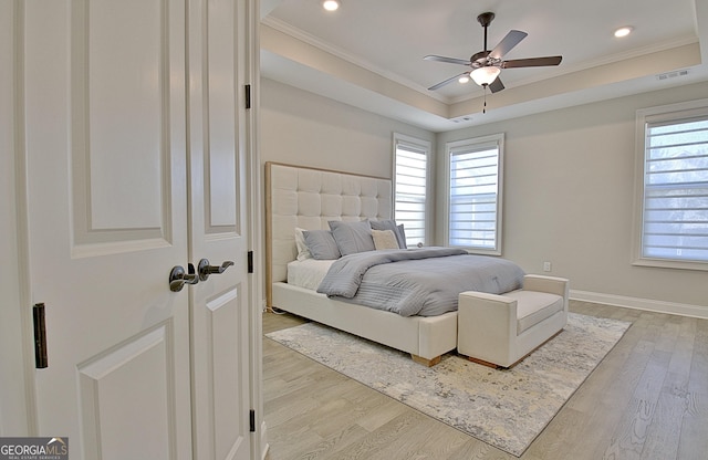 bedroom with ornamental molding, ceiling fan, light wood-type flooring, and a tray ceiling