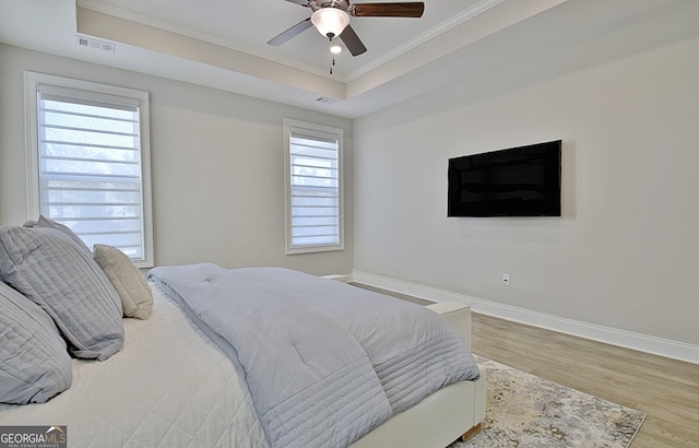 bedroom with crown molding, hardwood / wood-style floors, ceiling fan, and a tray ceiling