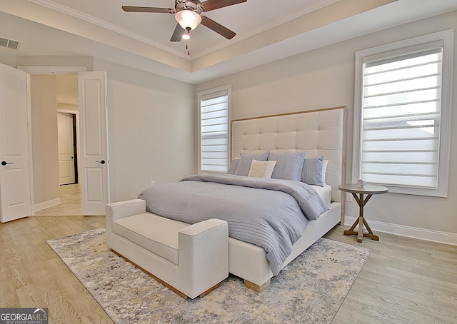 bedroom with multiple windows, crown molding, a tray ceiling, and light wood-type flooring