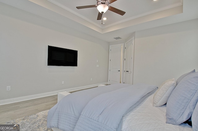 bedroom with crown molding, ceiling fan, a raised ceiling, and light hardwood / wood-style flooring