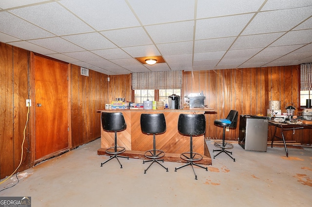 bar with a drop ceiling, stainless steel refrigerator, and wood walls