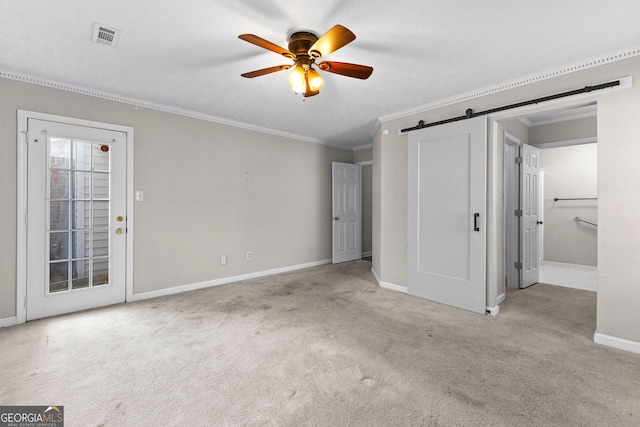 unfurnished bedroom featuring ceiling fan, light colored carpet, ornamental molding, and a barn door