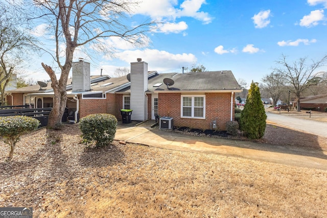 back of house with brick siding, central AC unit, a chimney, and a shingled roof