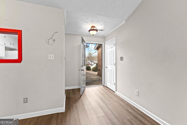 foyer featuring a textured ceiling, visible vents, wood finished floors, baseboards, and ornamental molding