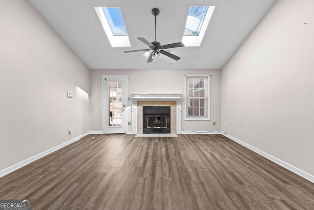 unfurnished living room with wood finished floors, baseboards, lofted ceiling with skylight, ceiling fan, and a tile fireplace
