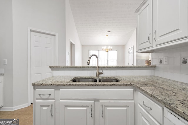 kitchen with sink, backsplash, light stone countertops, a textured ceiling, and white cabinets