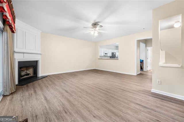 unfurnished living room featuring hardwood / wood-style floors, a large fireplace, and ceiling fan