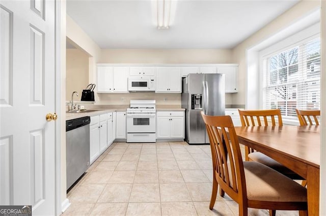 kitchen with appliances with stainless steel finishes, sink, light tile patterned floors, and white cabinets