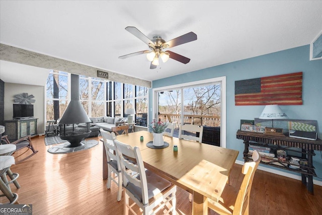 dining space with ceiling fan, hardwood / wood-style floors, and a wood stove