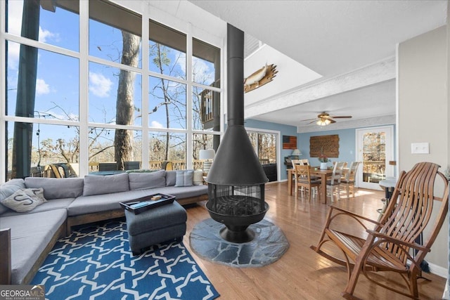 living room with a towering ceiling, hardwood / wood-style floors, a wood stove, a wall of windows, and ceiling fan