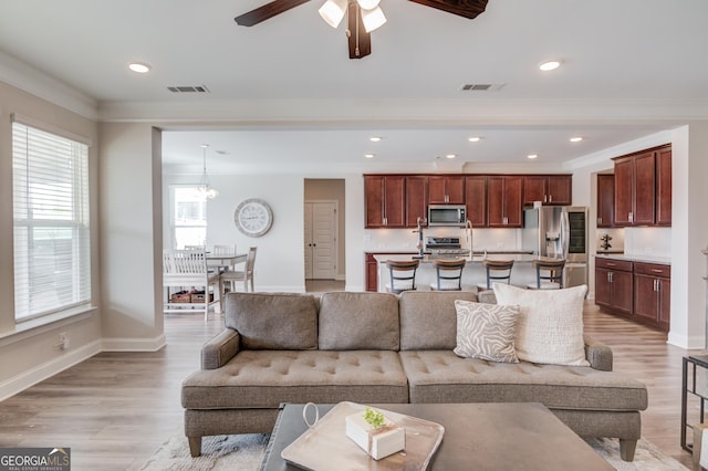 living room featuring light wood-type flooring, crown molding, and ceiling fan