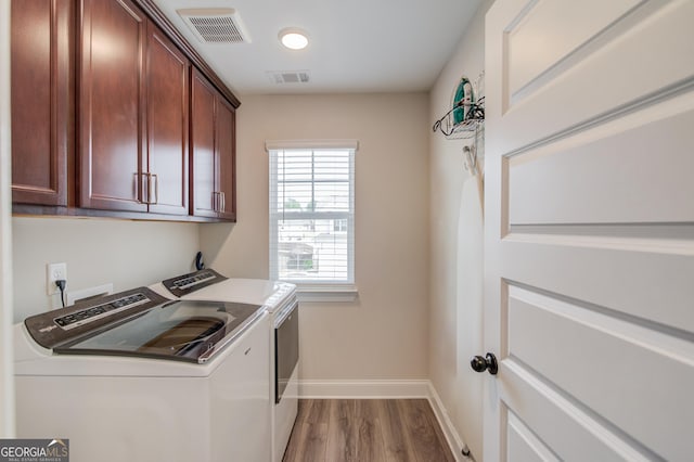 clothes washing area featuring washing machine and clothes dryer, wood-type flooring, and cabinets