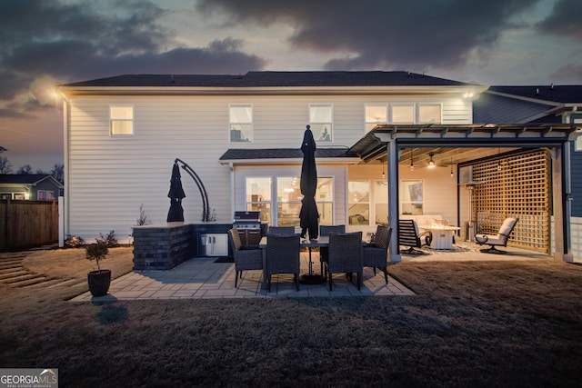 back house at dusk featuring a patio area and an outdoor kitchen