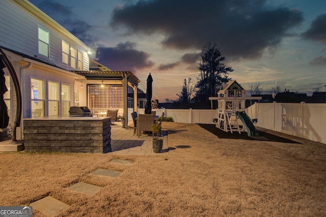 yard at dusk with a patio, a playground, and exterior kitchen