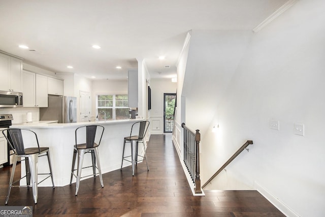 kitchen with dark wood-type flooring, a breakfast bar area, white cabinetry, stainless steel appliances, and decorative backsplash